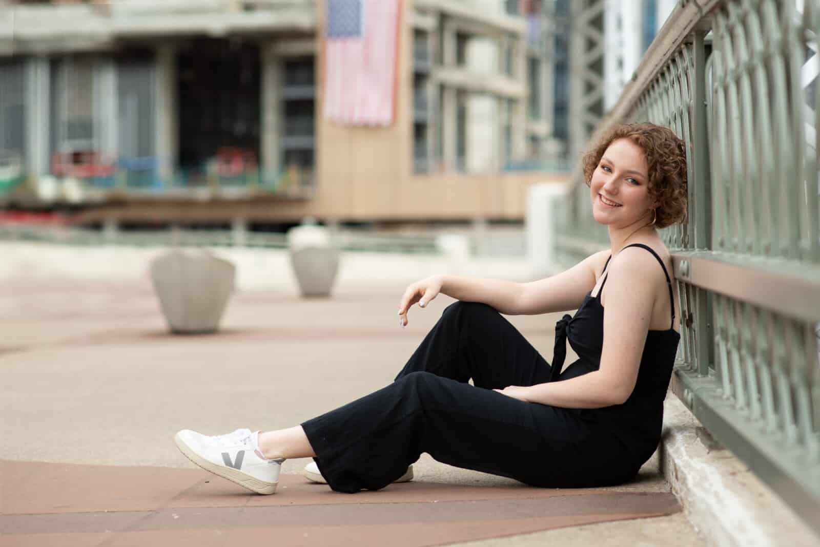 senior girl leaning back on bridge wearing black jumpsuit